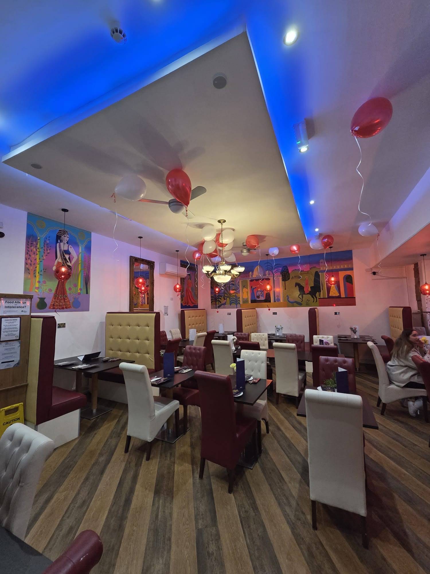 Sultan of Keswick dining room, with colourful wall art, red and cream chairs, hanging lights and balloons
